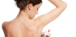 young woman applying deodorant, studio white